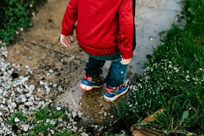 Child splashing water on a sidewalk with rocks and grass