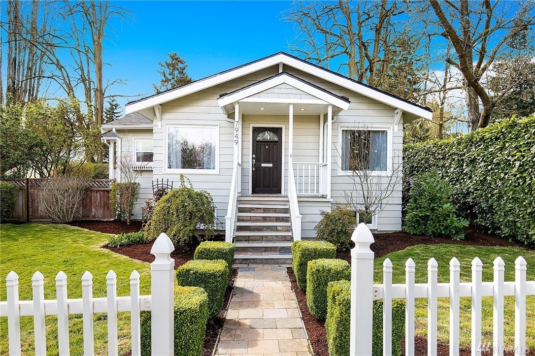 White craftsman home with white picket fence and shrubbery