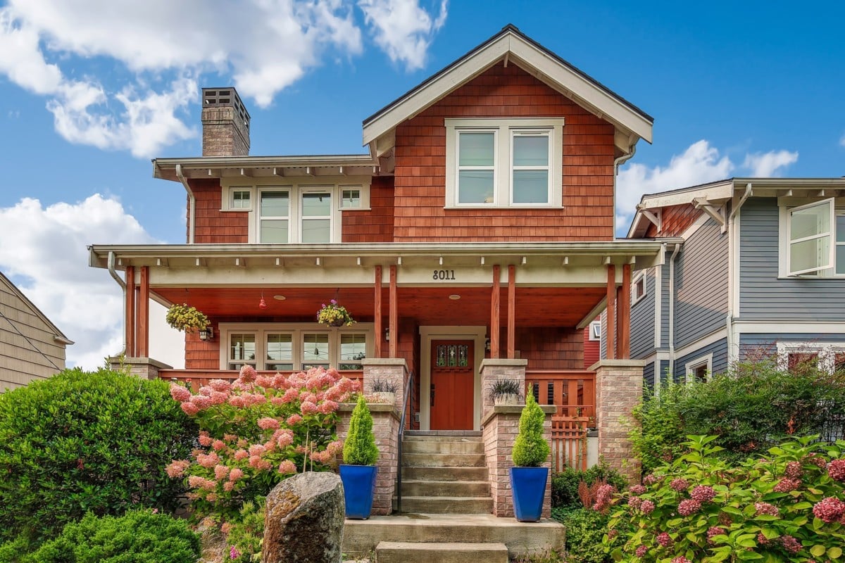 Two-story red brick colored craftsman home with greenery