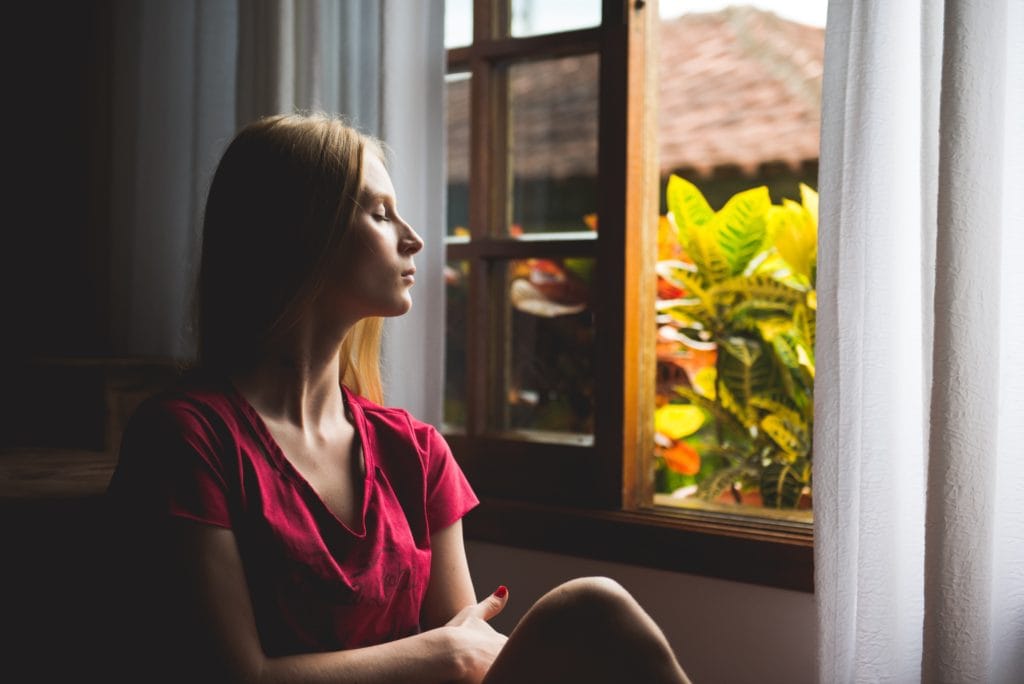 woman meditating at home by window