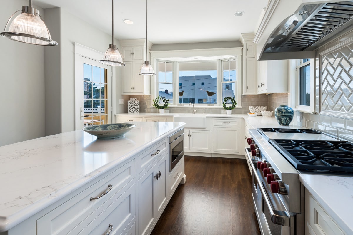 A clean kitchen with stainless steel appliances, white cabinets, and white quartz countertops