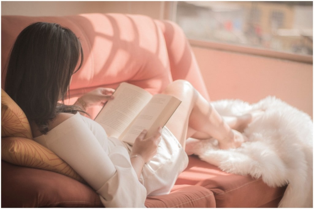 woman reading book on pink couch 