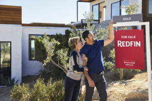 Couple standing outside of home recently purchased: learn how to choose a real estate agent