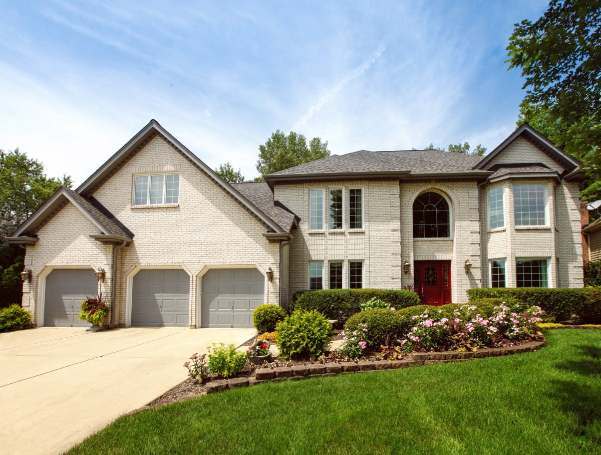White brick home with a red door and beautiful yard