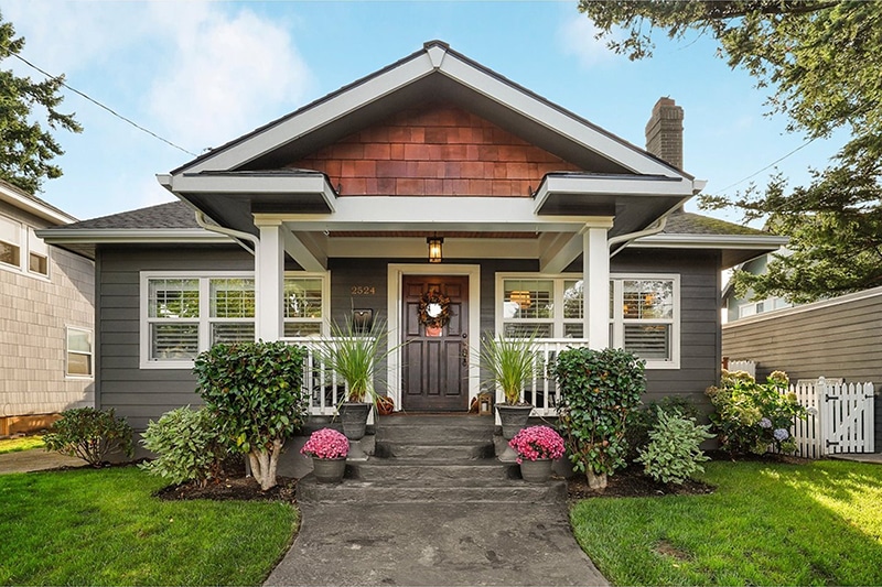 Green craftsman style home with front porch and beautiful landscaping