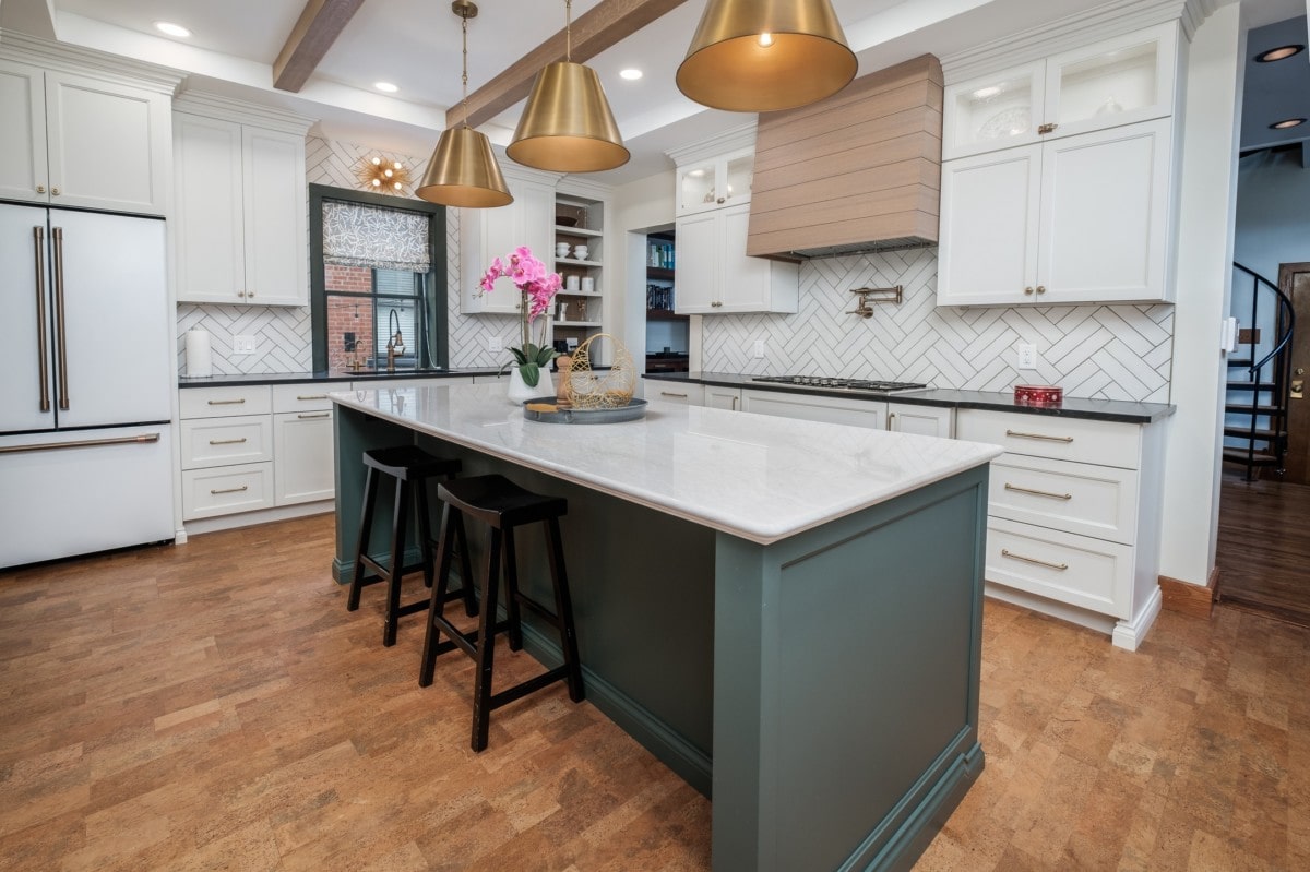 A kitchen with white cabinets, quartz countertops, gold pendant lights over a olive-painted island designed by a professional