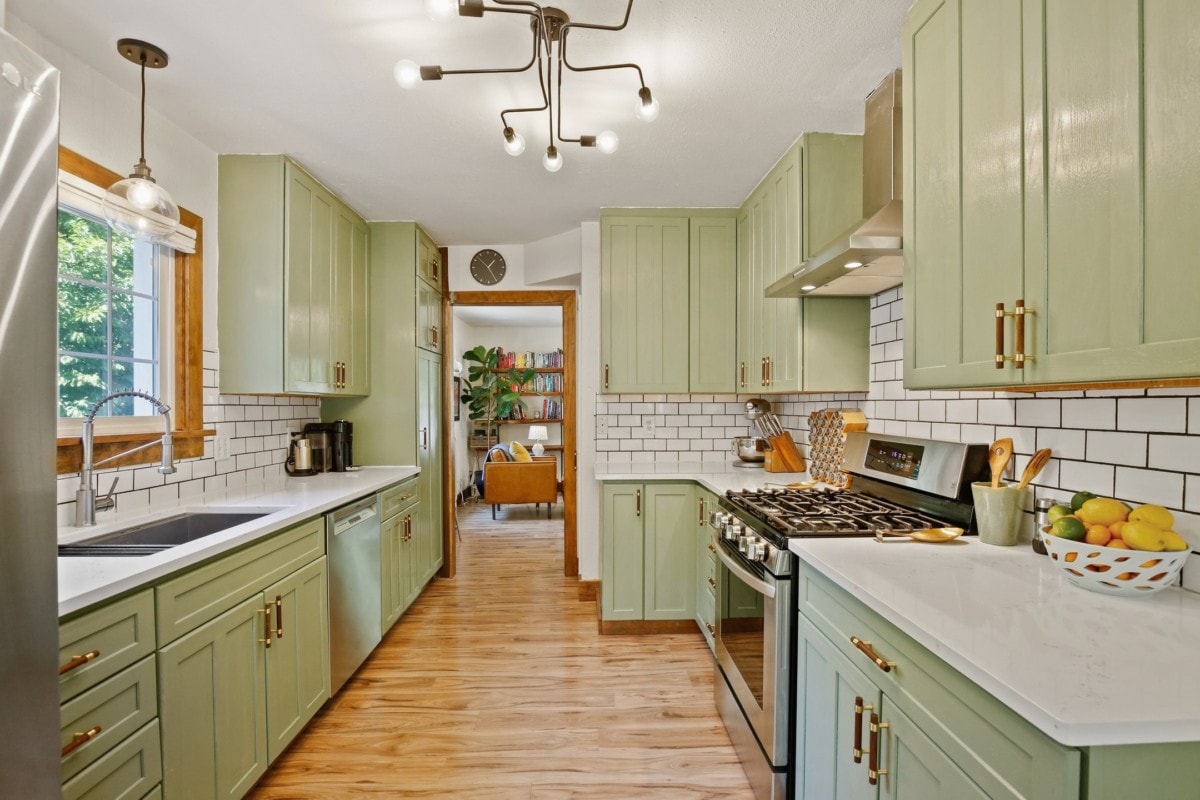 A beautiful green kitchen with wood floors and white countertops