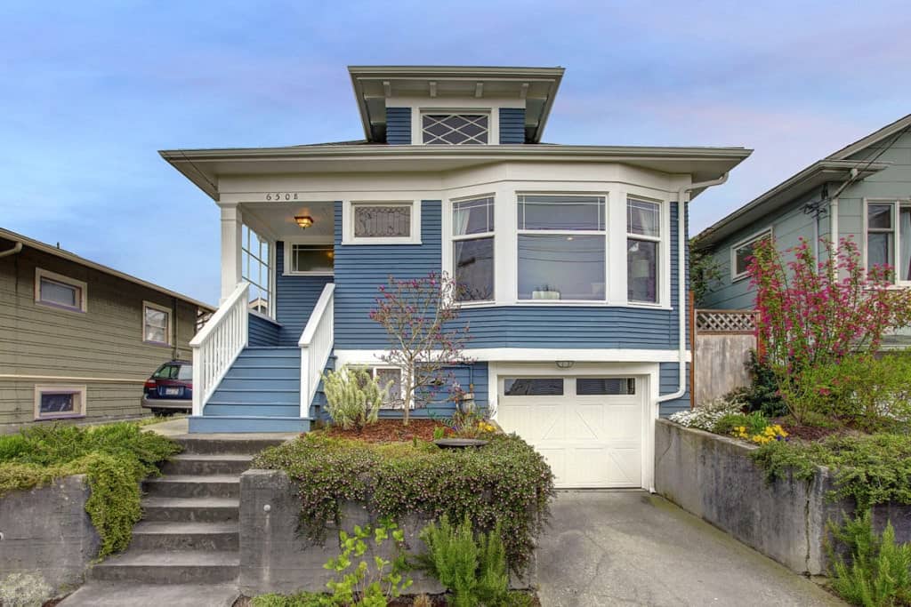A three-story blue home with white accents and a garage