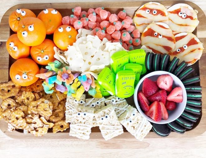 Halloween inspired snack board with pretzels, strawberries, oranges, and more