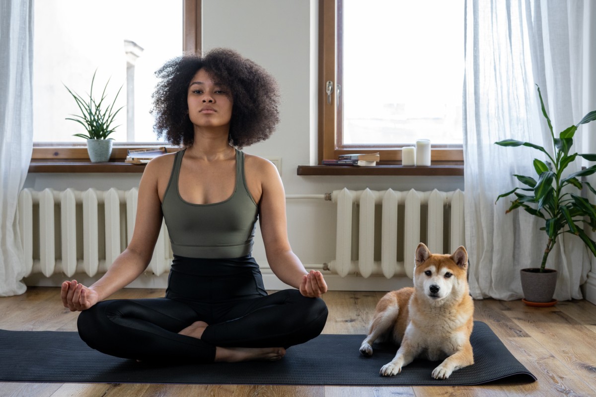 Person doing yoga at home on a yoga mat with their dog