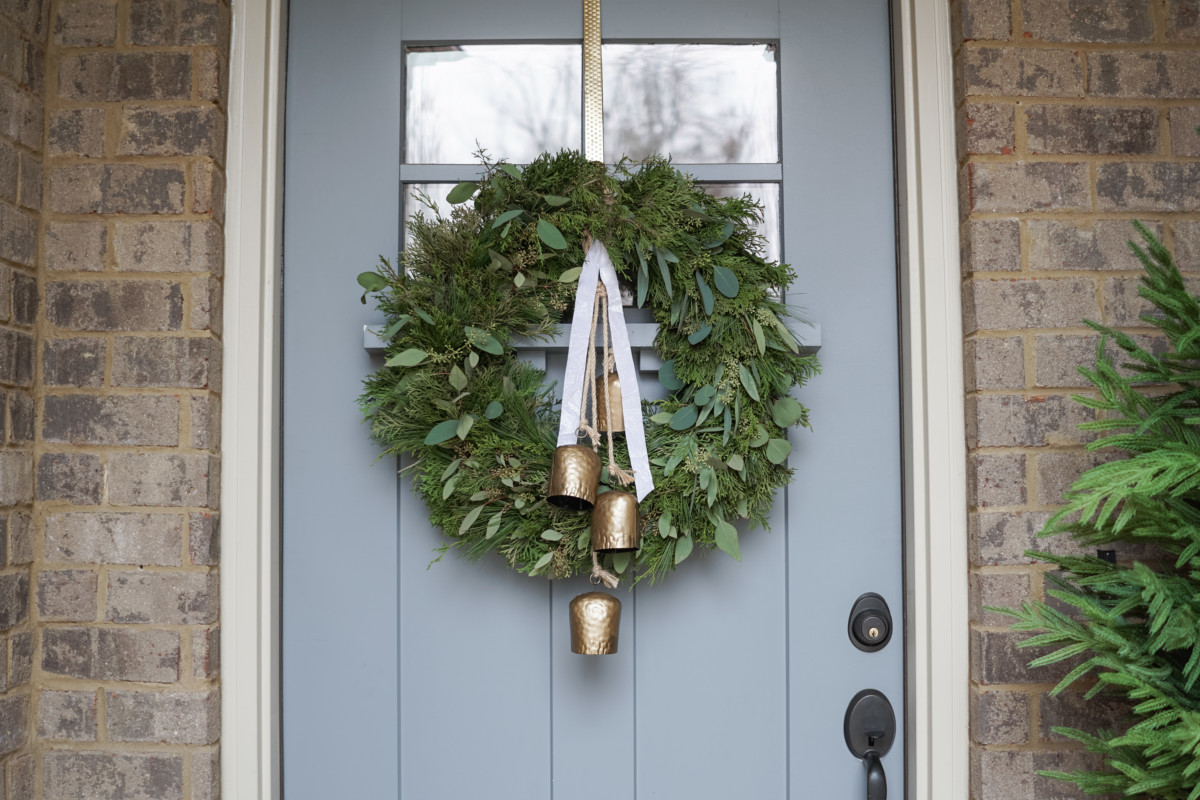 wreath on the front door with white ribbon and three bells
