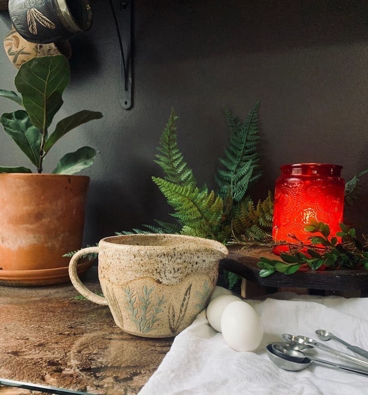 ceramic mug on a table with plants and a candle behind it