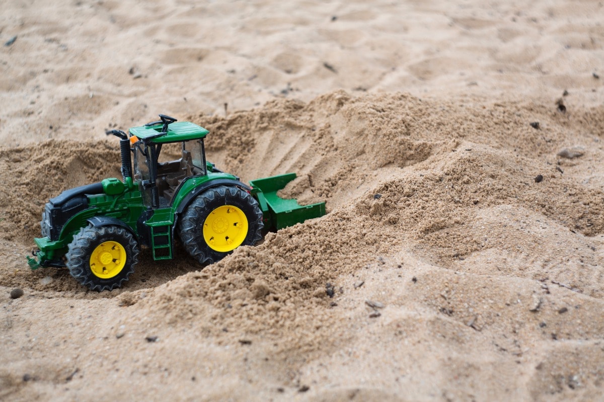 A green toy tractor in the sand