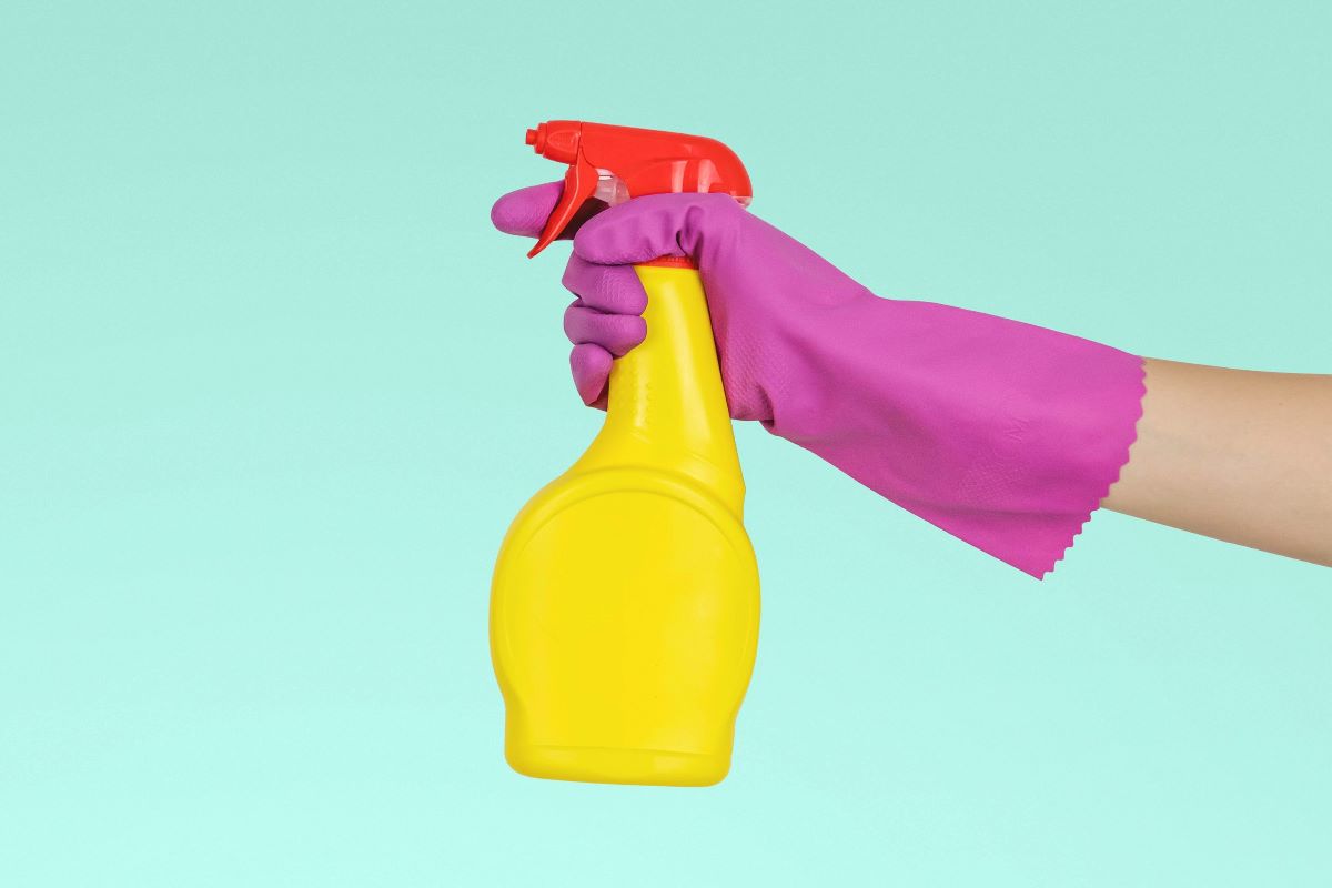 gloved hand holding a yellow spray bottle