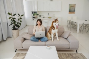 A woman sitting with a laptop on her knees beside her dog