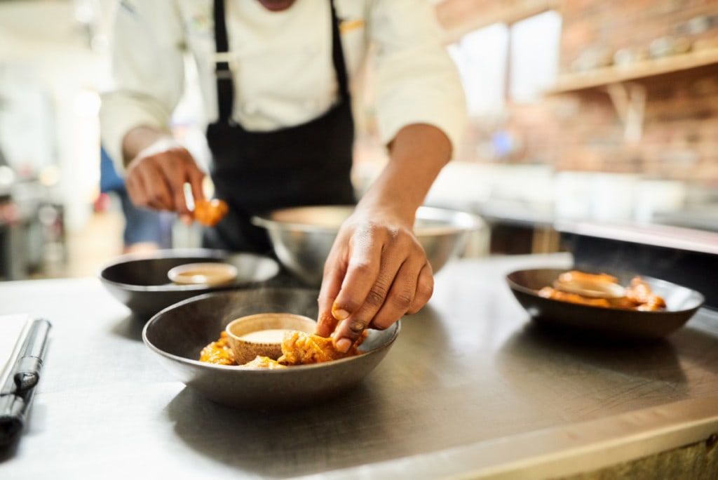 Detailný záber na mužského šéfkuchára aranžujúceho jedlo na tanieri v komerčnej kuchyni