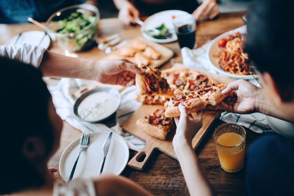 Close up of a young group of friends passing and serving food while enjoying together. They are having fun, chatting and feasting on food and drinks at dinner party Getty