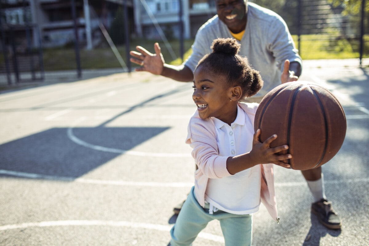 Close up of a grandfather taking his granddaughter to play some basketball in the park _ getty