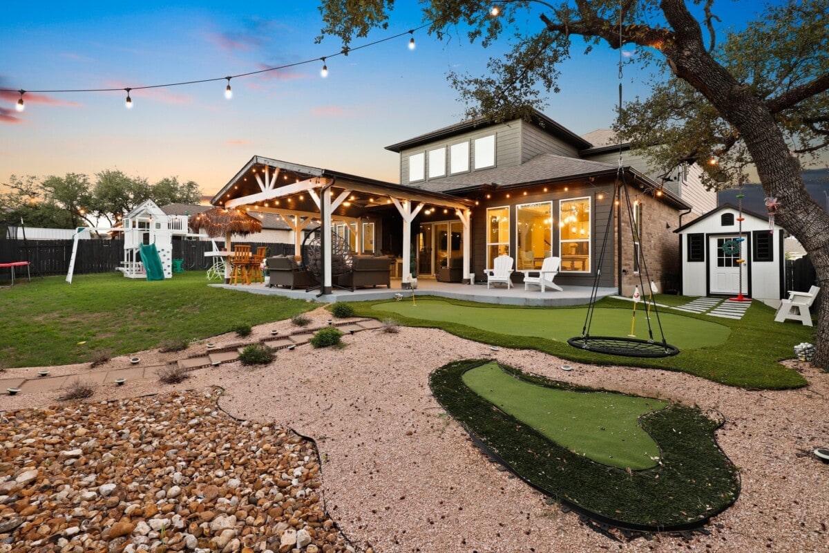 large fenced backyard with putting green and covered patio