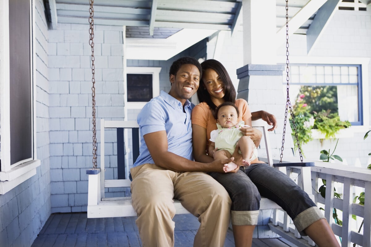 A family sitting together on a large light blue, front porch swing