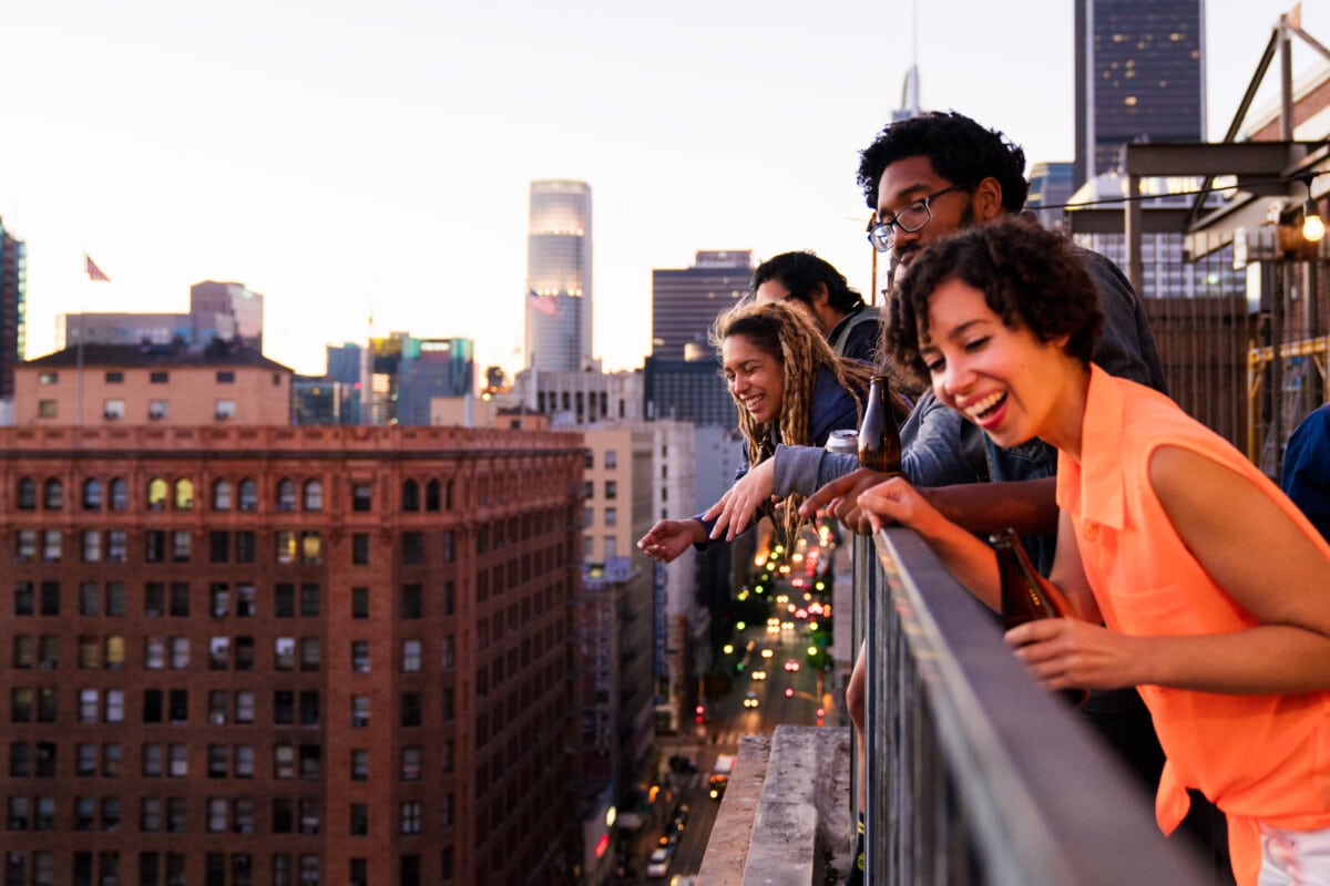 Group of friends hanging out together on a balcony in downtown Los Angeles, looking over the side down towards the street. Los Angeles _ getty