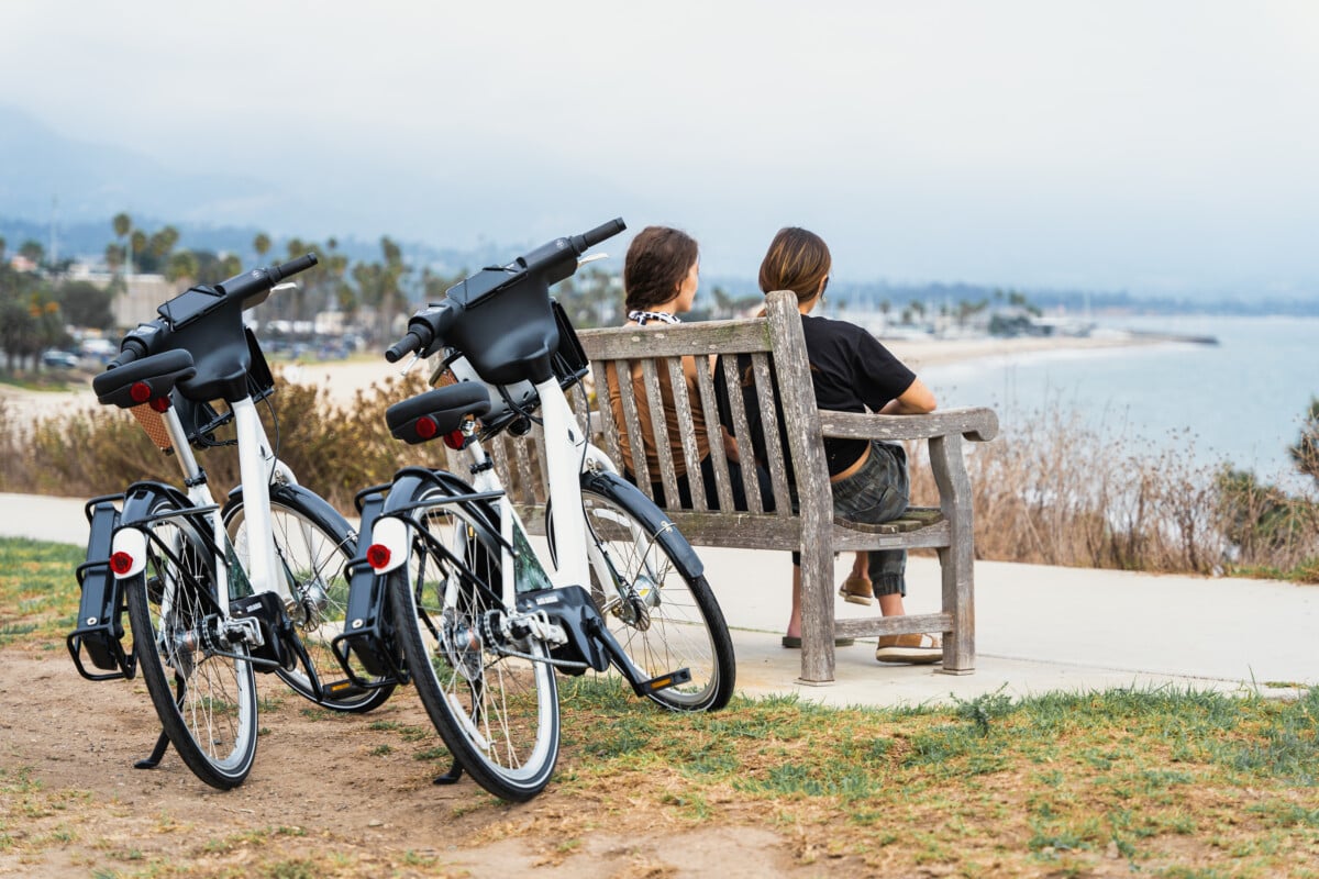 two people on a bench overlooking santa barbara with electric bikes behind them