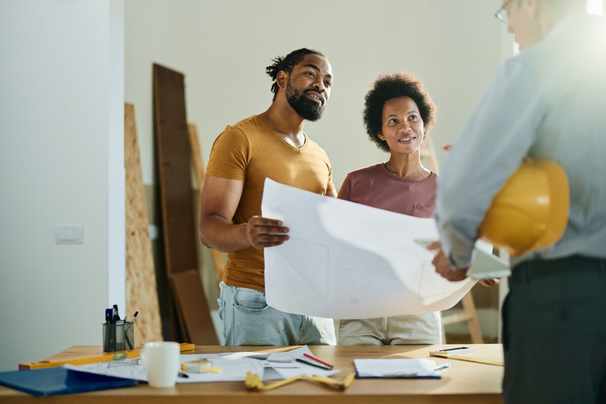 couple talking to real estate agent in the apartment. while holding plans