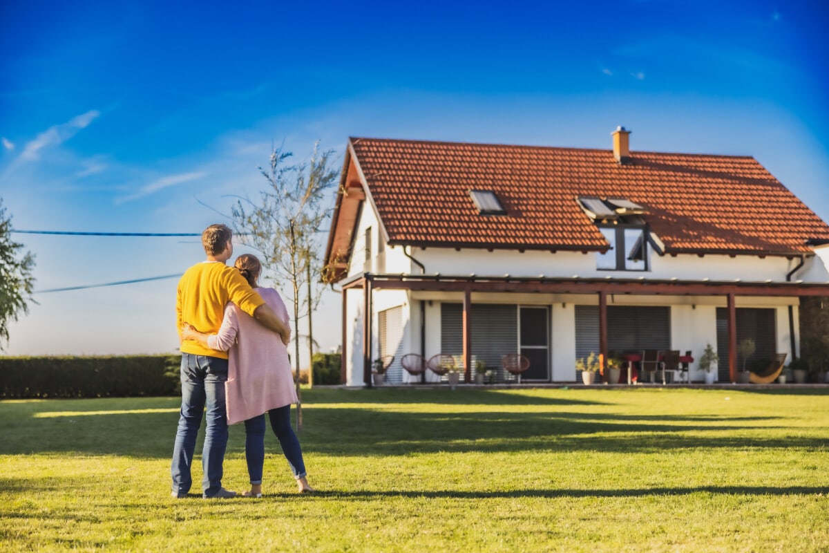 Man and woman,hugging each other while standing on the lawn in the backyard of their new bought house,rear view,modern house in the background 