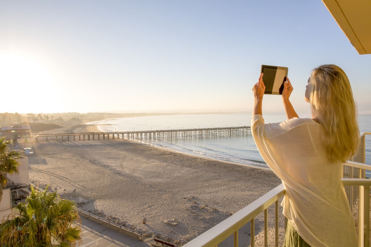 Woman takes photo with digital tablet on balcony over ocean