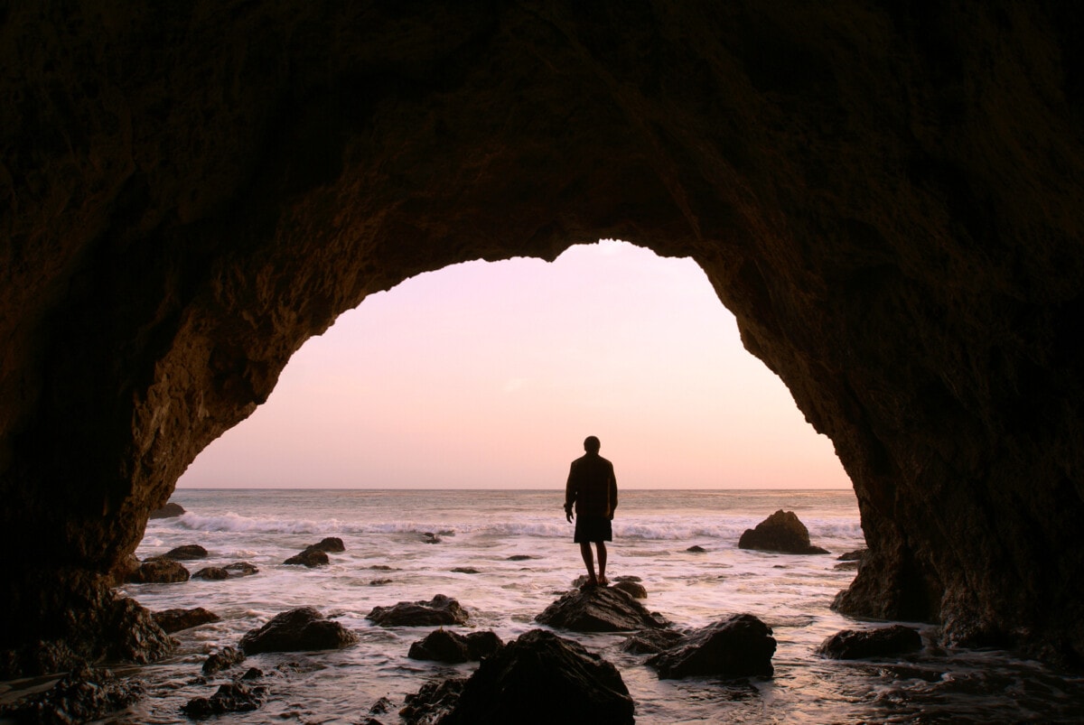 silhouette man standing in sea cave at sunset
