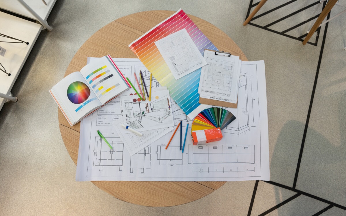 Blueprints, sketches, color swatches, pencil colors and designs on table.