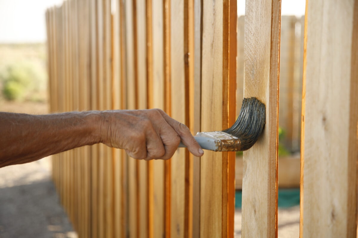 Applying weather proofing treatment to a cedar picket fence.