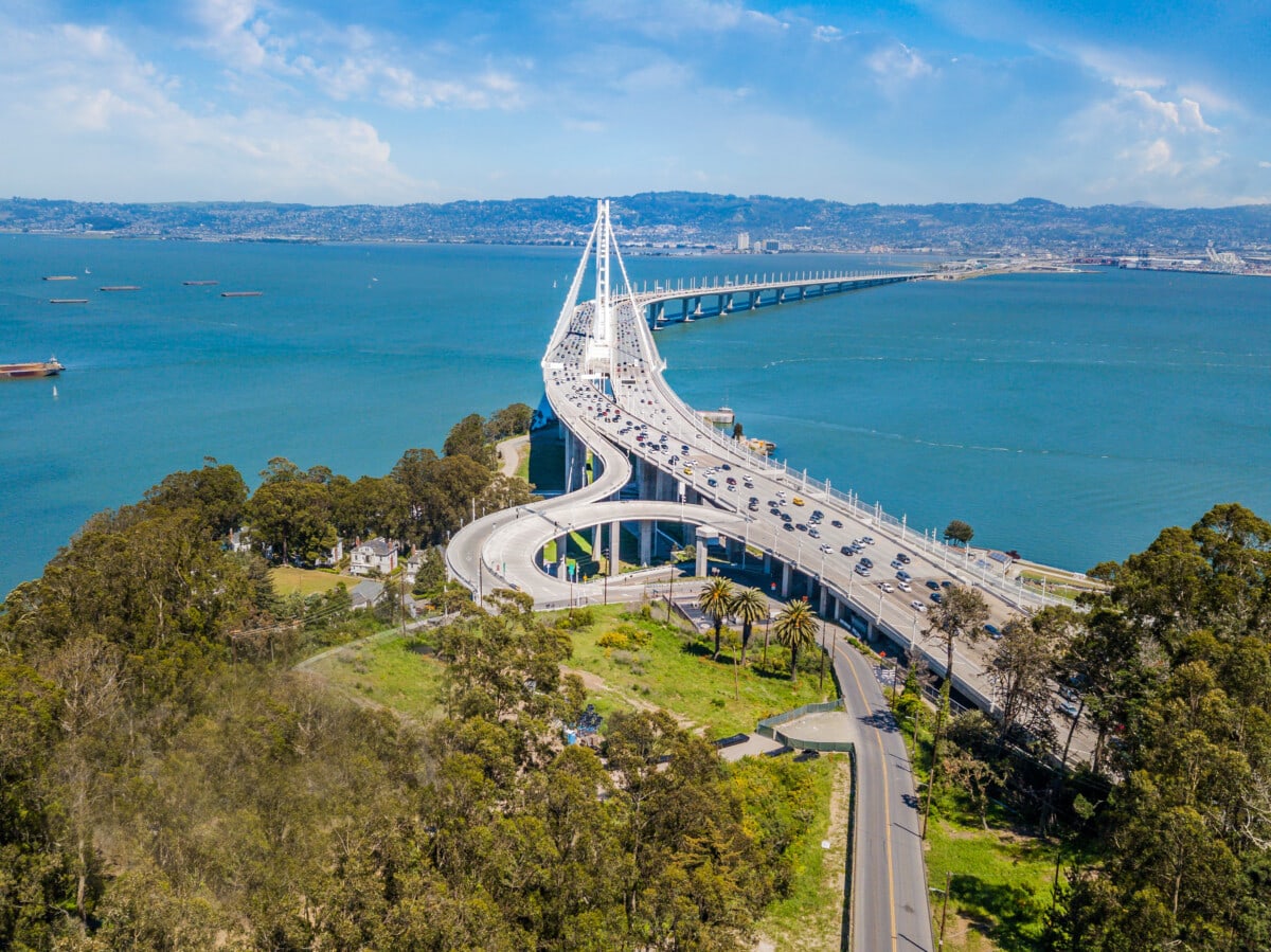 An aerial view of the Bay Bridge on a sunny day. A view from Treasure Island looking across the bay at Emeryville and Oakland. Ships and boats are in the Bay.