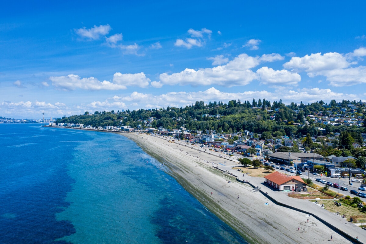 Alki Beach in Seattle with the tide out.  People walk along the waterfront path in the summer and enjoy the beach.