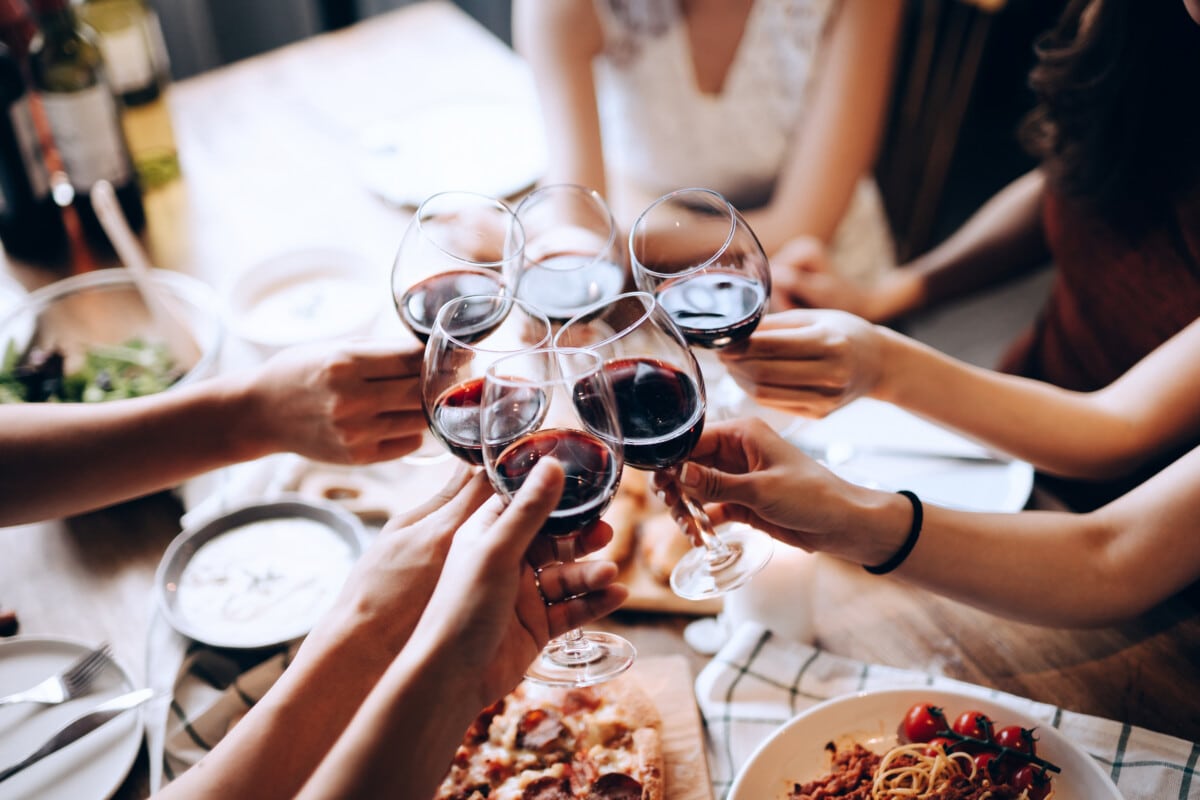 Close up shot of a group of joyful friends enjoying together, having fun and toasting with red wine during dinner party