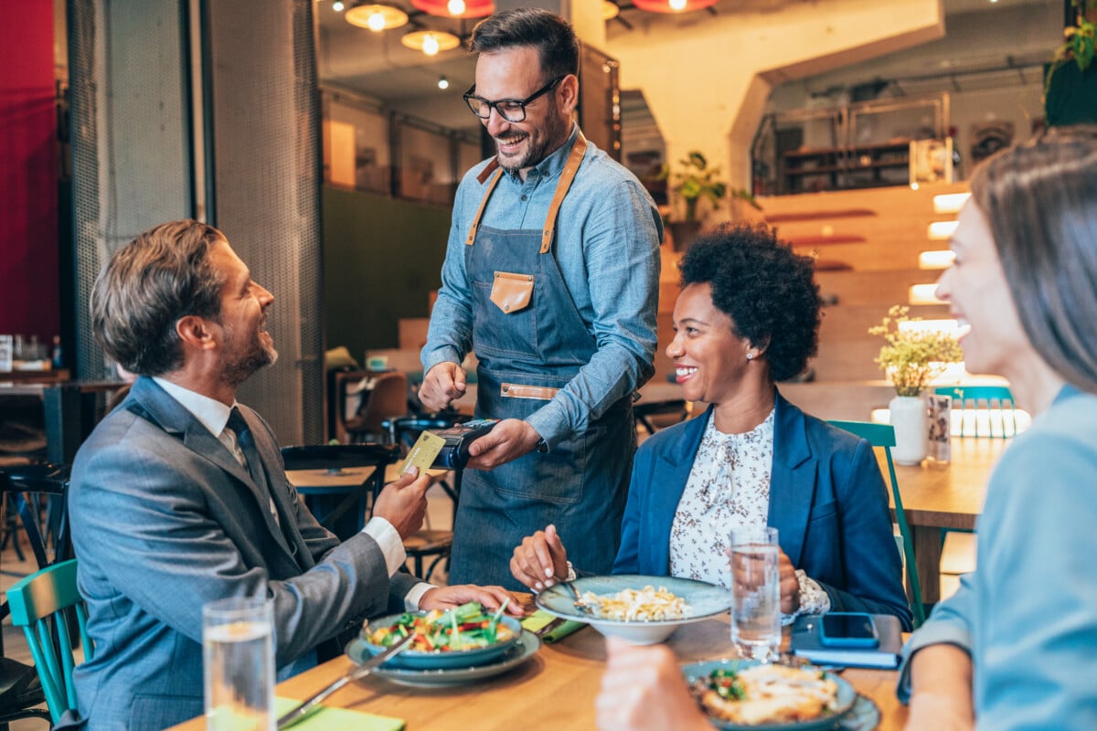 Businessman paying for a lunch with business colleagues. A diverse group of businesspeople enjoying lunch at a restaurant, and businessman paying with a credit card via contactless payment