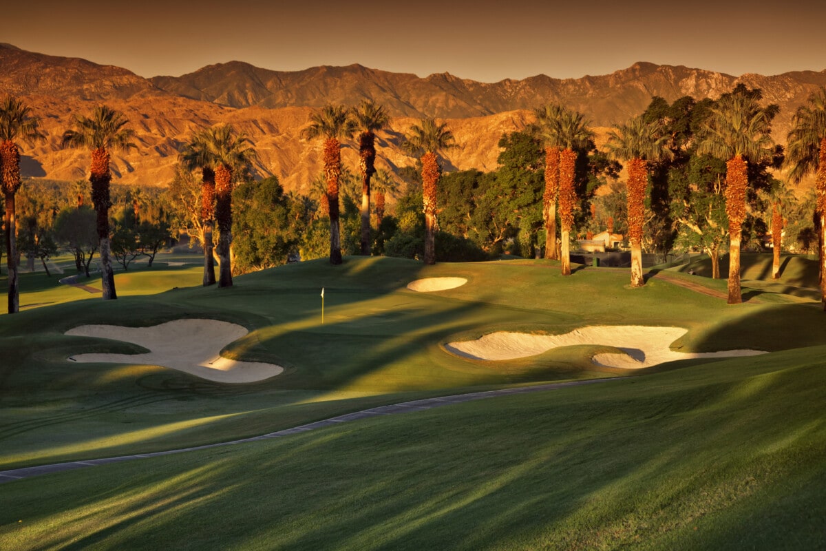 Picturesque Golf Green surrounded by mountains and Palm trees at sunrise.