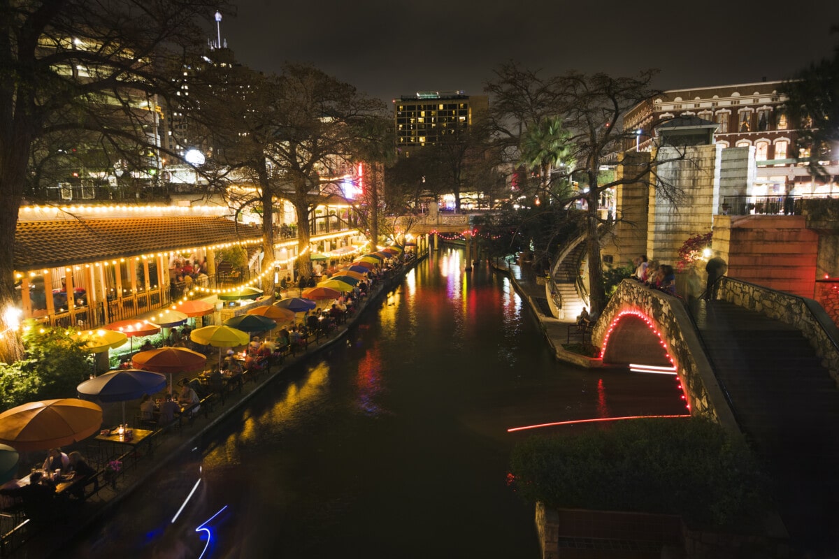 Cafes and bridges lit up with festive lights, showing the night life at the Riverwalk entertainment district in downtown San Antonio, Texas, USA.