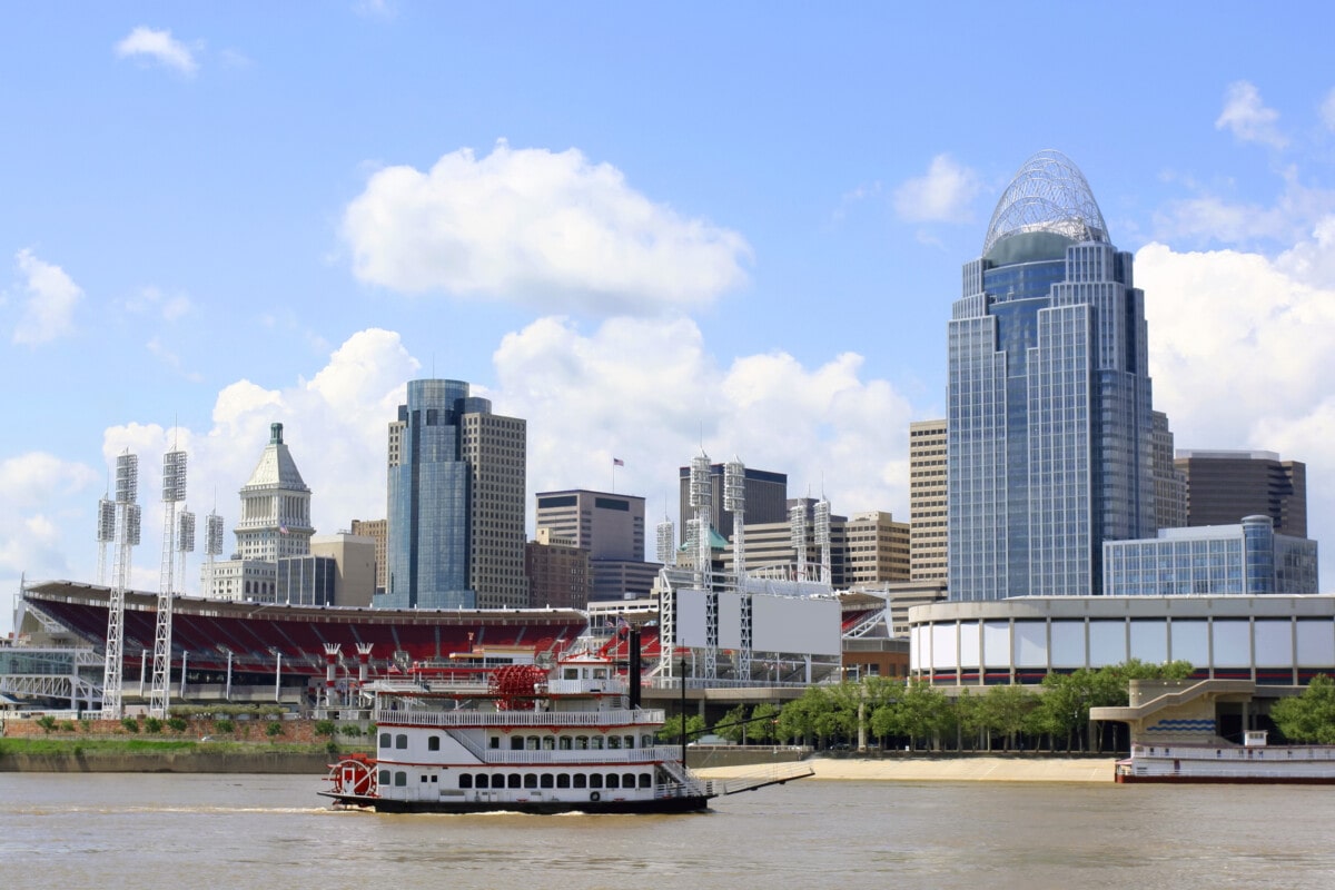 The Ohio River on a sunny day with the skyline of the city of Cincinnati in the background. A steamboat sails by in the foreground. Shot in 2011 and includes the Queen City Tower, completed in 2011.