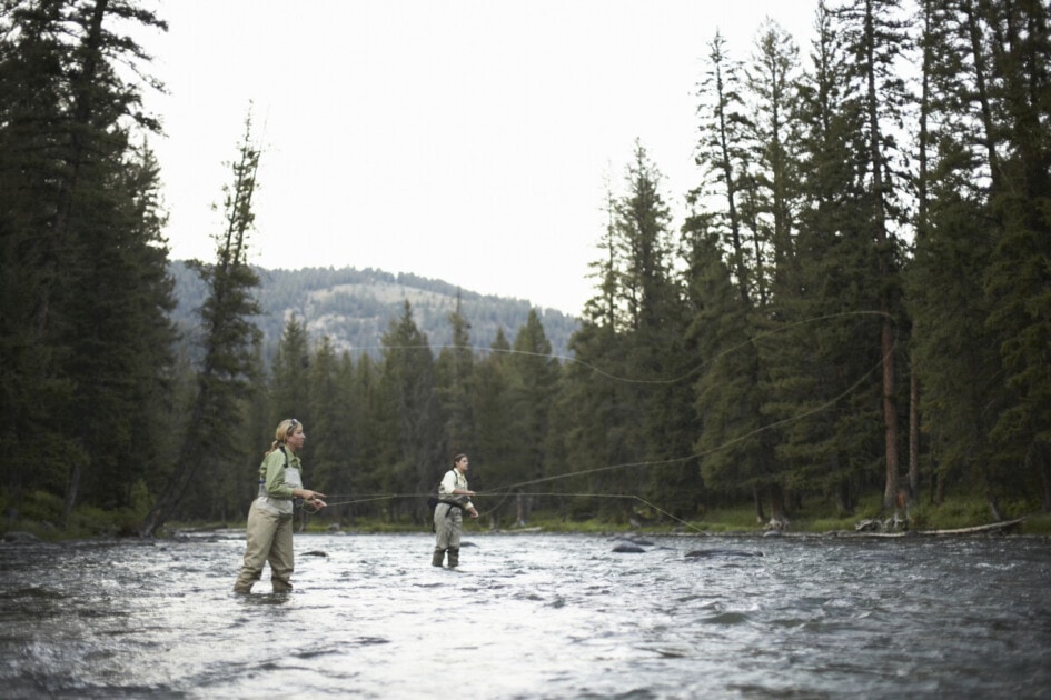 Two women fly-fishing in river, side view