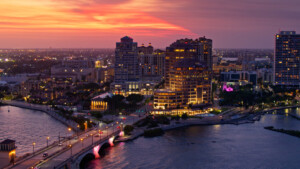 Aerial establishing shot of West Palm Beach, Florida at dusk on a spring evening, looking across Lake Worth Lagoon and Royal Park Bridge towards hotels and condo towers