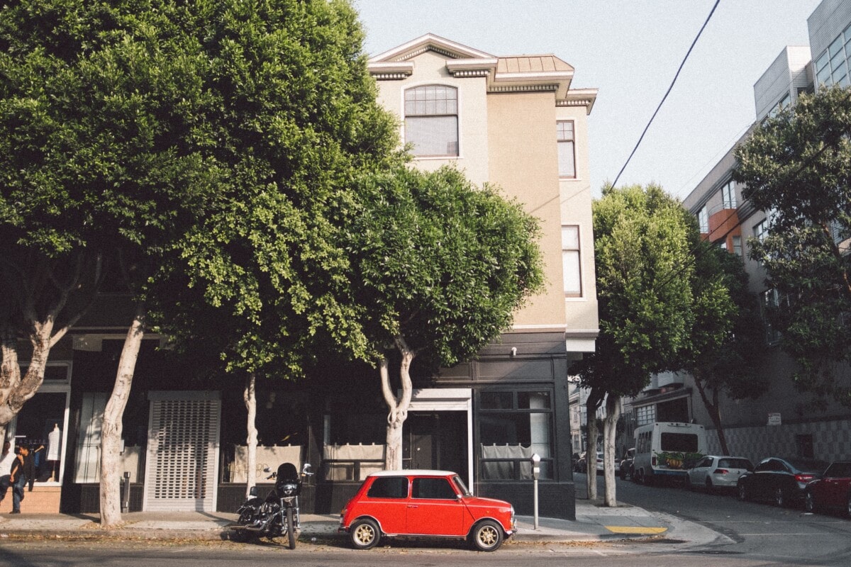 corner street with bright red car and large lush tree in San Francisco