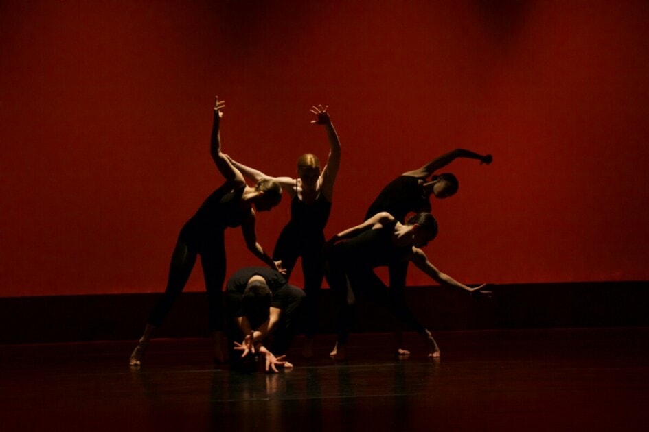 Five dancers are backlit against a red curtain.