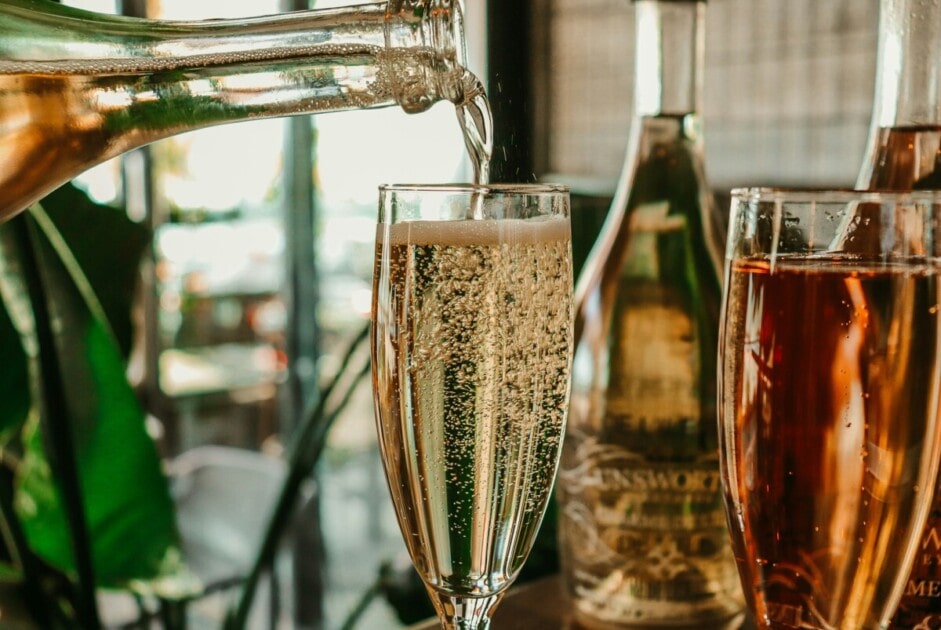 A bottle of sparkling wine is poured into a tall glass.