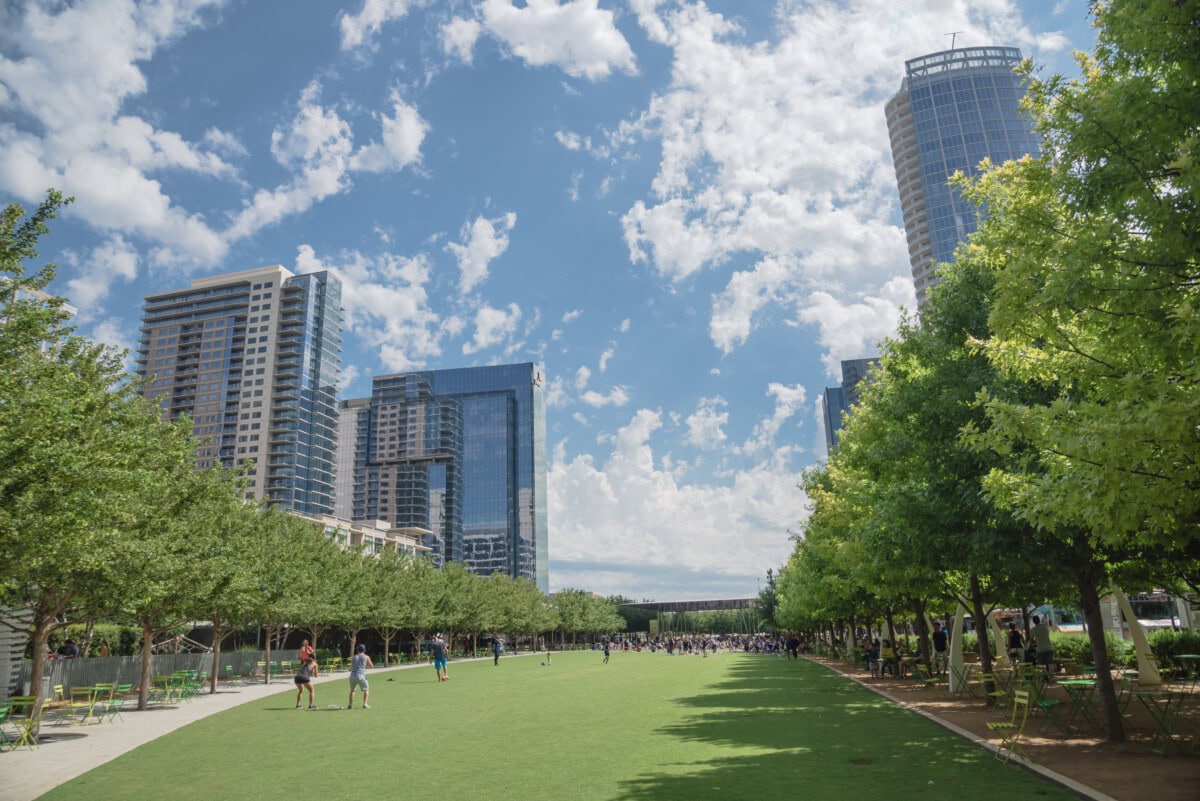 DALLAS, TX, USA-MAY 26, 2018:Klyde Warren Park, a 5.2-acre public park in downtown Dallas, Texas. People playing sport on green lawn grass under sunny day cloud blue sky. Live oak tree and skyscraper