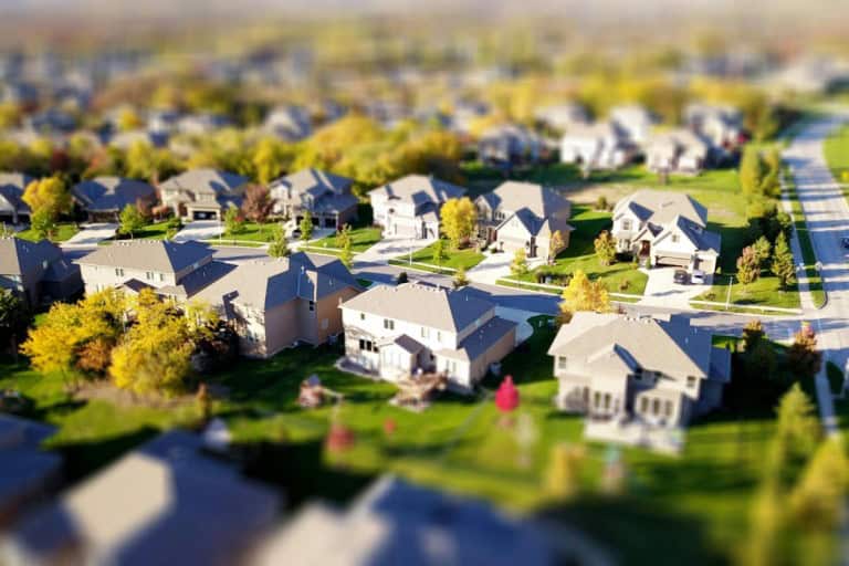 Aerial view of a planned suburban residential neighborhood with numerous modern houses and green lawns, representing communities that may be governed by both CDD and HOA regulations, with a tilt-shift effect making the scene appear miniature.