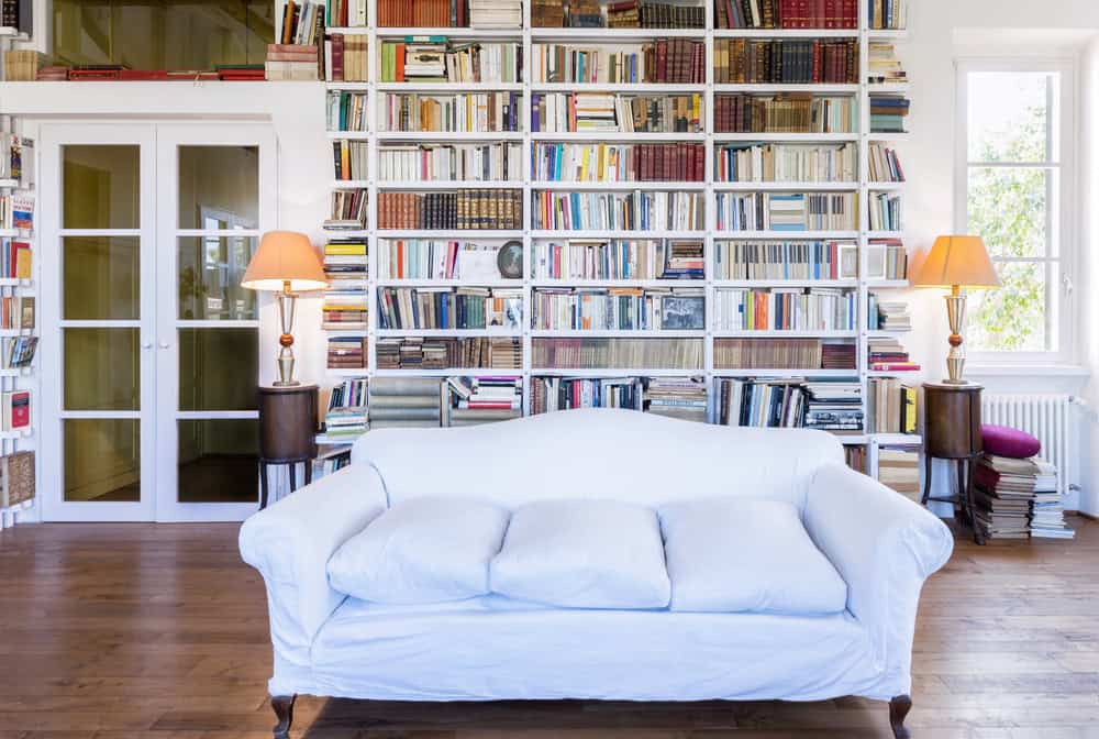 bright, cozy at home library with white couch in the center and shelves lined with books