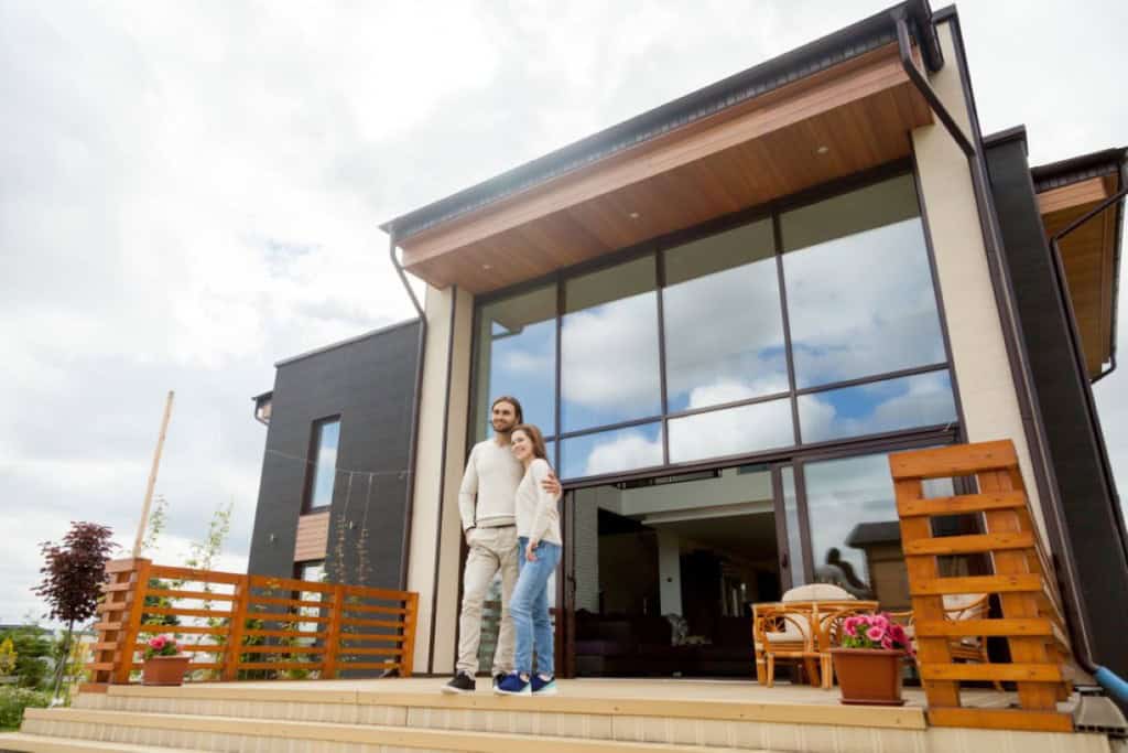 Smiling couple standing outside their modern home after completing a pre-listing inspection to prepare for sale.