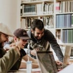 Use Redfin to learn how to rent an apartment as an international student. A group of students are gathered around a laptop in a study hall. They are laughing together.