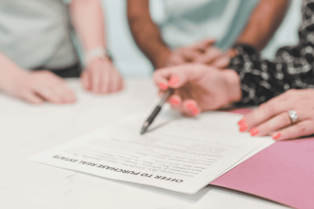 A real estate agent reviewing and signing an offer to purchase real estate document with clients — illustrating key steps on how to convince a seller to accept your offer.